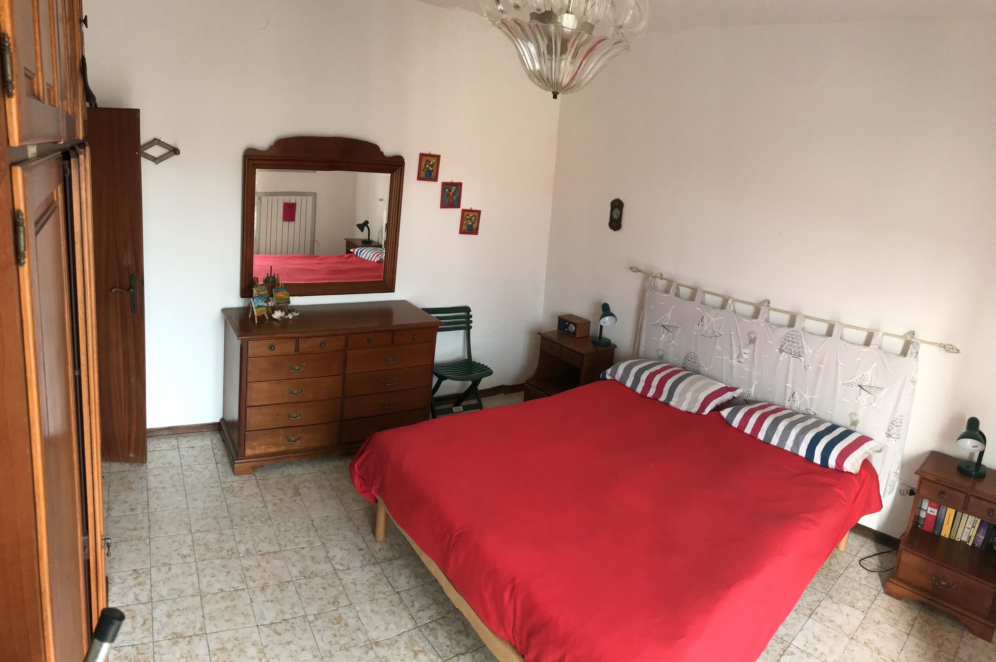 Ein Schlafzimmer mit Bett, Kommode, Spiegel und einem kleinen Tisch mit Büchern.