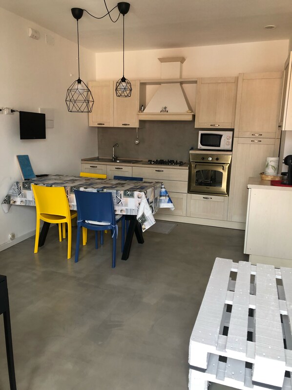 A modern kitchen with light wood cabinets, a built-in microwave, a stove, and a dining area with yellow and blue chairs.
