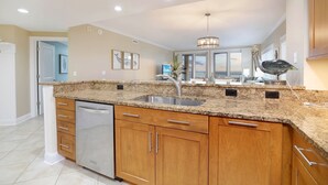 A kitchen with granite countertops, stainless steel appliances, wooden cabinets, and a pendant light. - Meridian 601 West by Seaside Vacations & Sales (Ocean City)