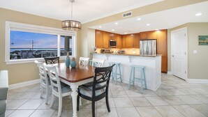 A modern kitchen with wooden cabinets, a stainless steel refrigerator, and a large island with bar stools. - Meridian 601 West by Seaside Vacations & Sales (Ocean City)