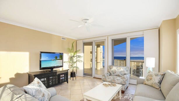 A living room with a television, sofa, coffee table, and a view of the ocean through large sliding doors. - Meridian 601 West by Seaside Vacations & Sales (Ocean City)
