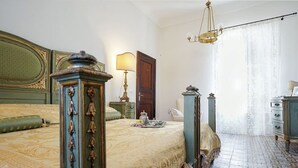 A bedroom with a large bed, a nightstand, a dresser, and a chandelier. - Antica Dimora La Portazza (Marsala)