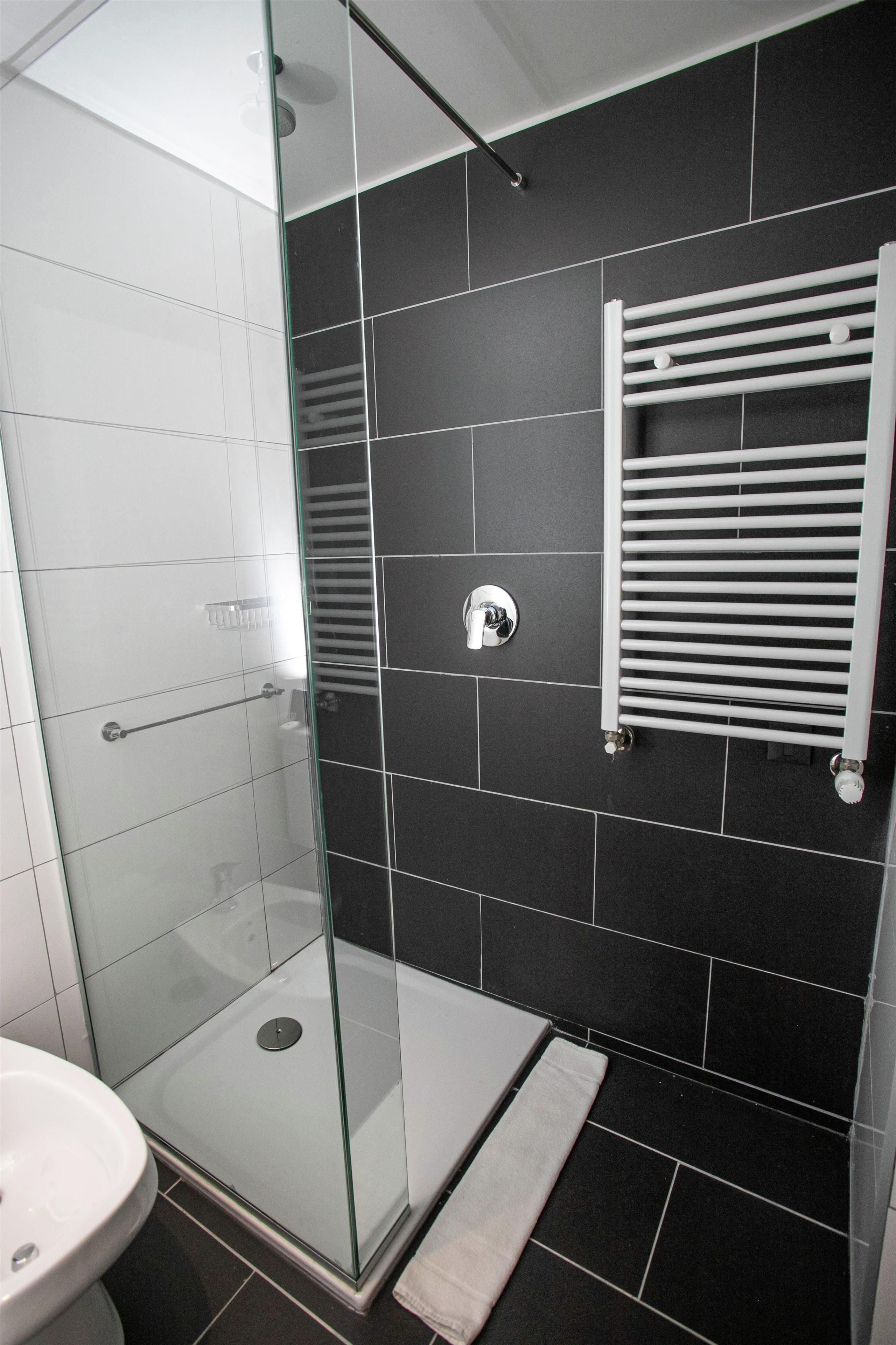 Ein modernes Badezimmer mit einer Duschkabine aus Glas, einem weißen Waschbecken und einem Handtuchhalter.
