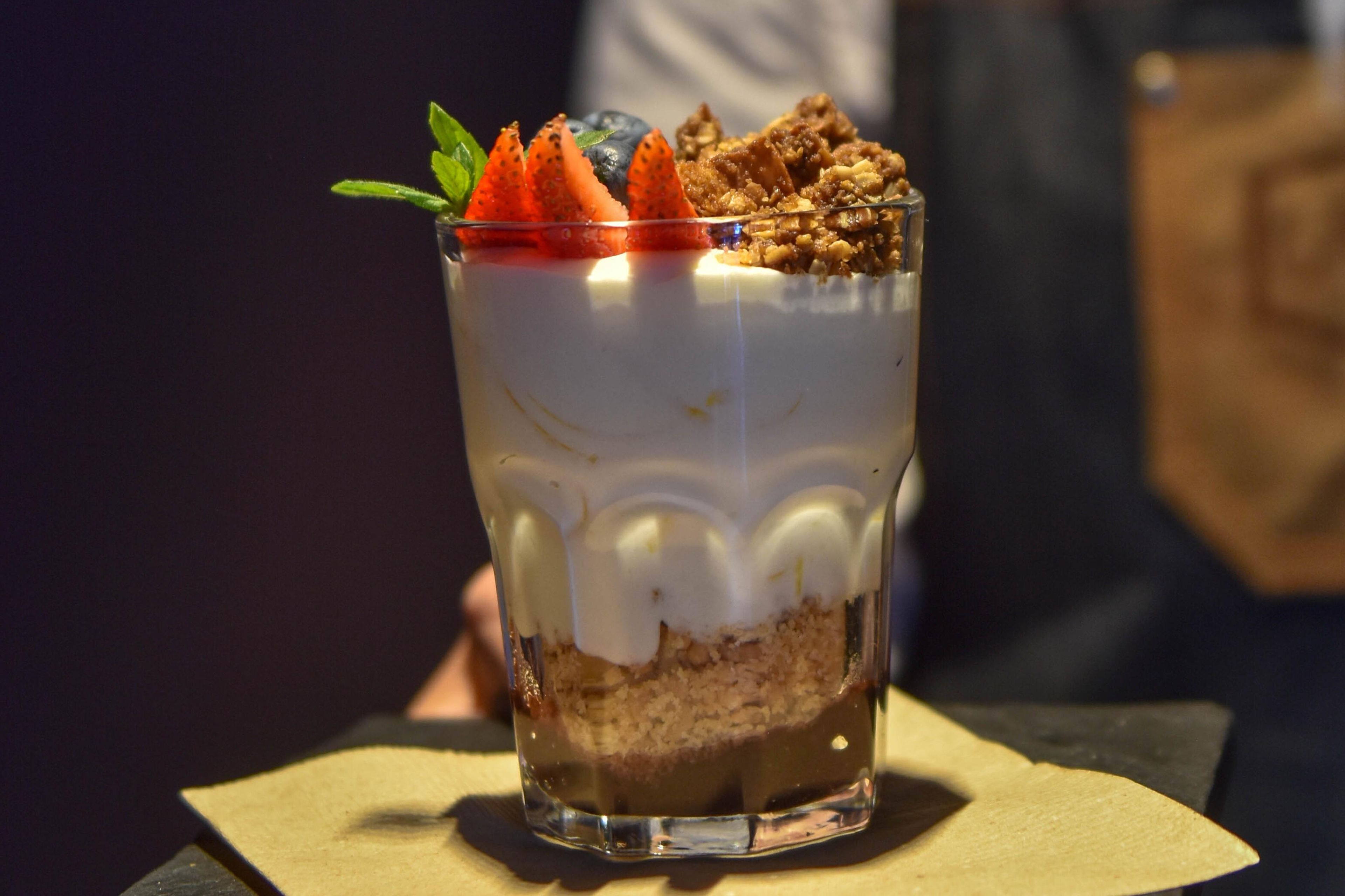 Un dessert composé de plusieurs couches, présenté dans un verre transparent, avec des fraises et du granola sur le dessus.