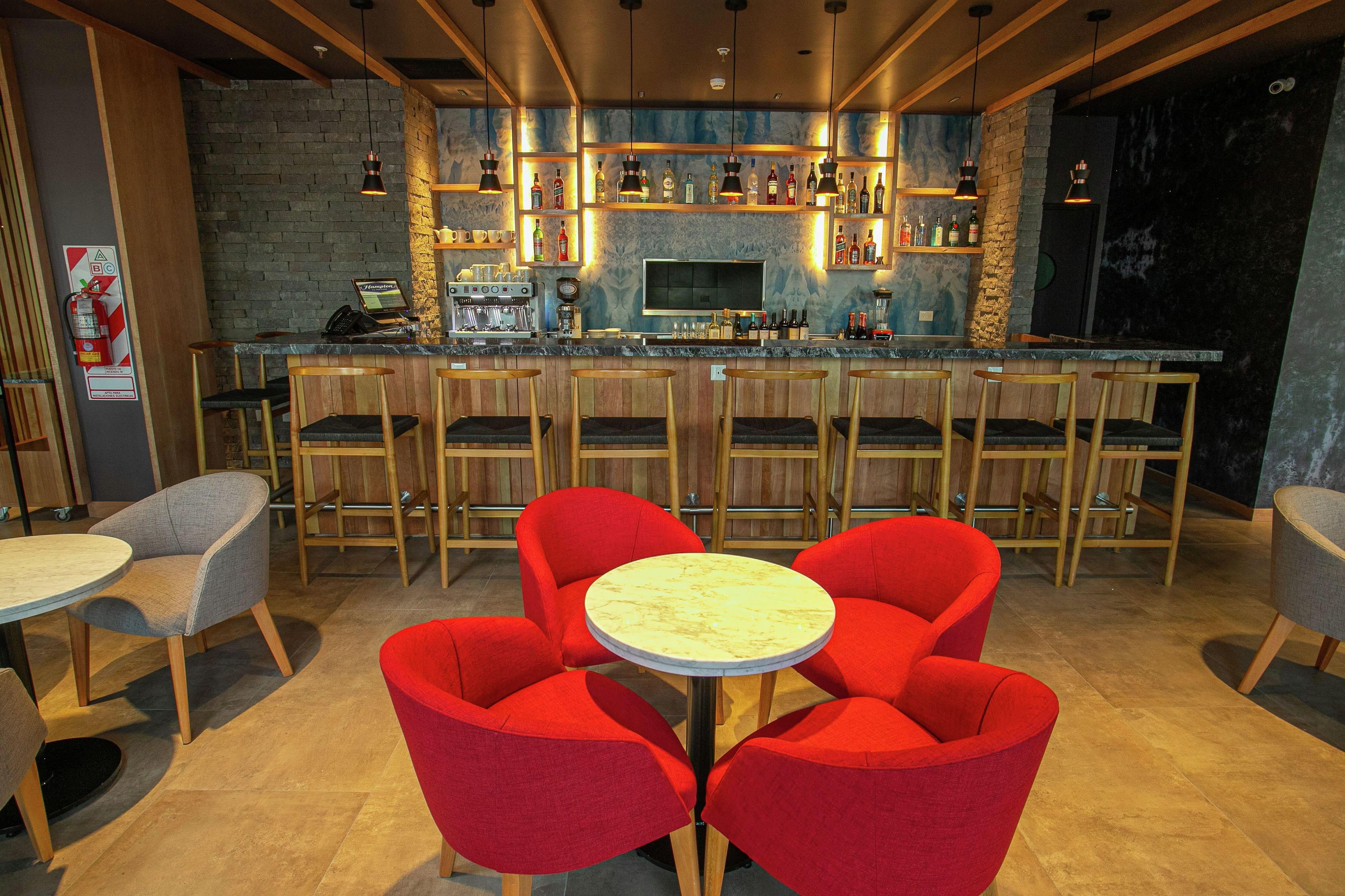 Een bar met houten stoelen, een toog en flessen op planken.