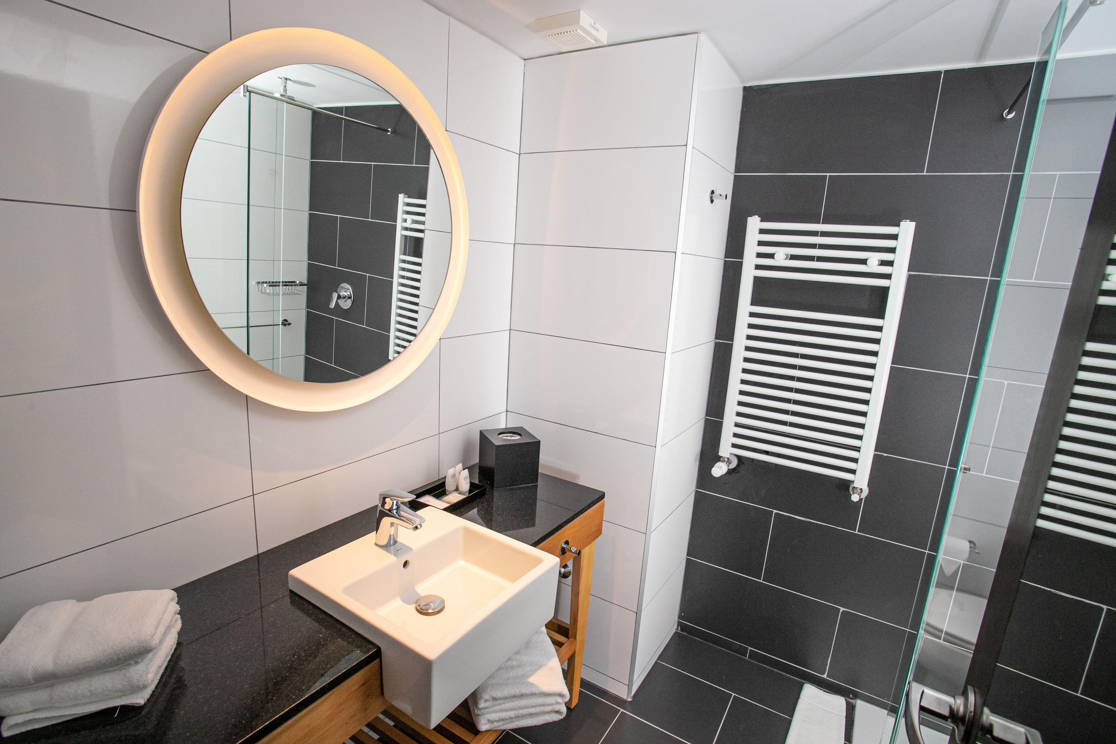 A modern bathroom with a round mirror, a sink, a glass shower enclosure, and a towel rack.