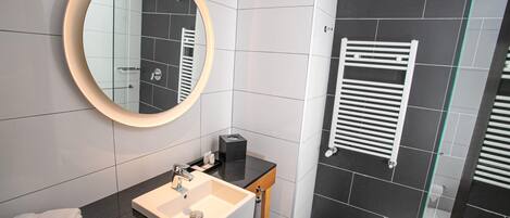 A modern bathroom with a round mirror, a sink, a glass shower enclosure, and a towel rack.