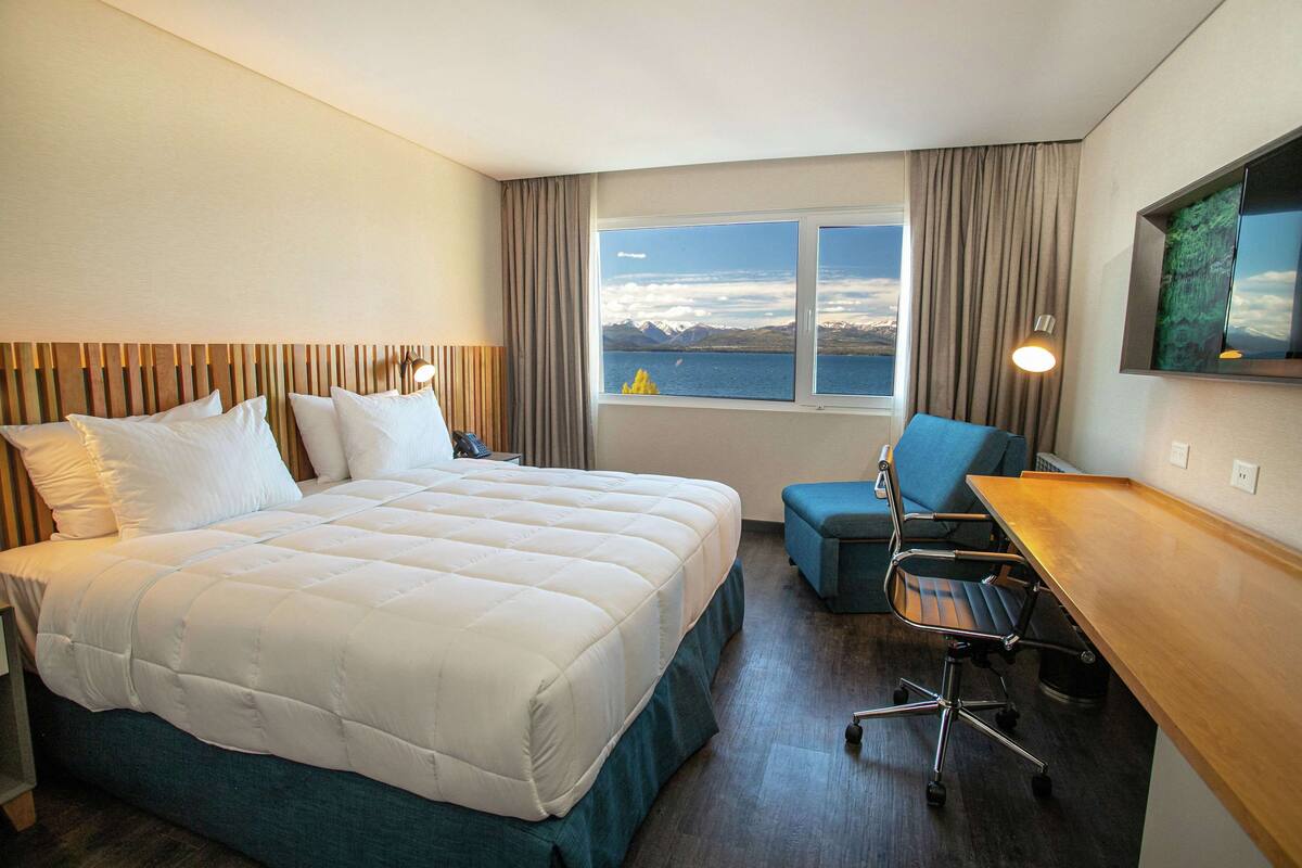 Habitación de hotel con cama, escritorio, silla, ventana con vistas y televisor de pantalla plana.