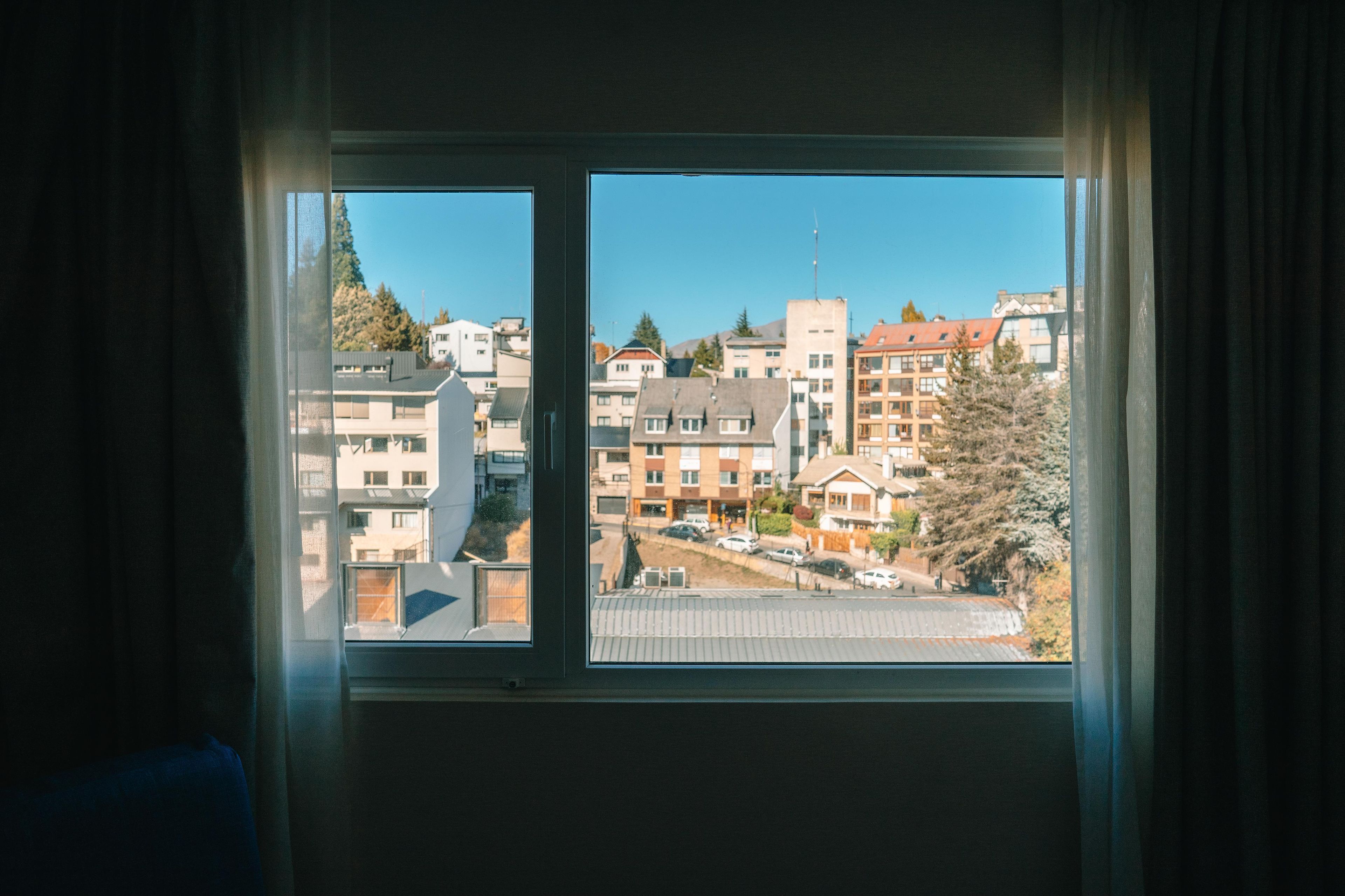 A window with a view of a residential area, including buildings and trees.