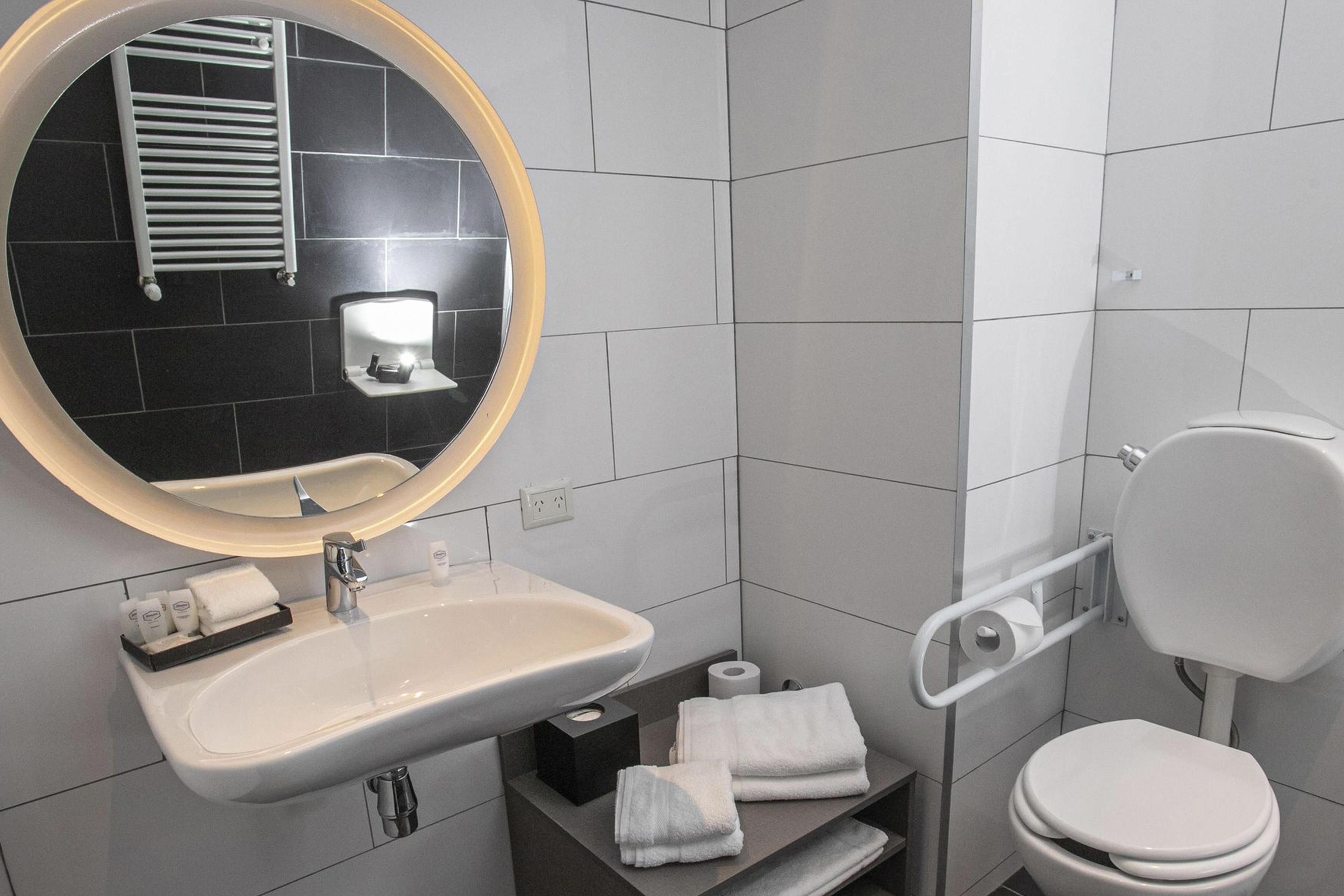 A modern bathroom with a round mirror, white sink, toilet, and towel rack.