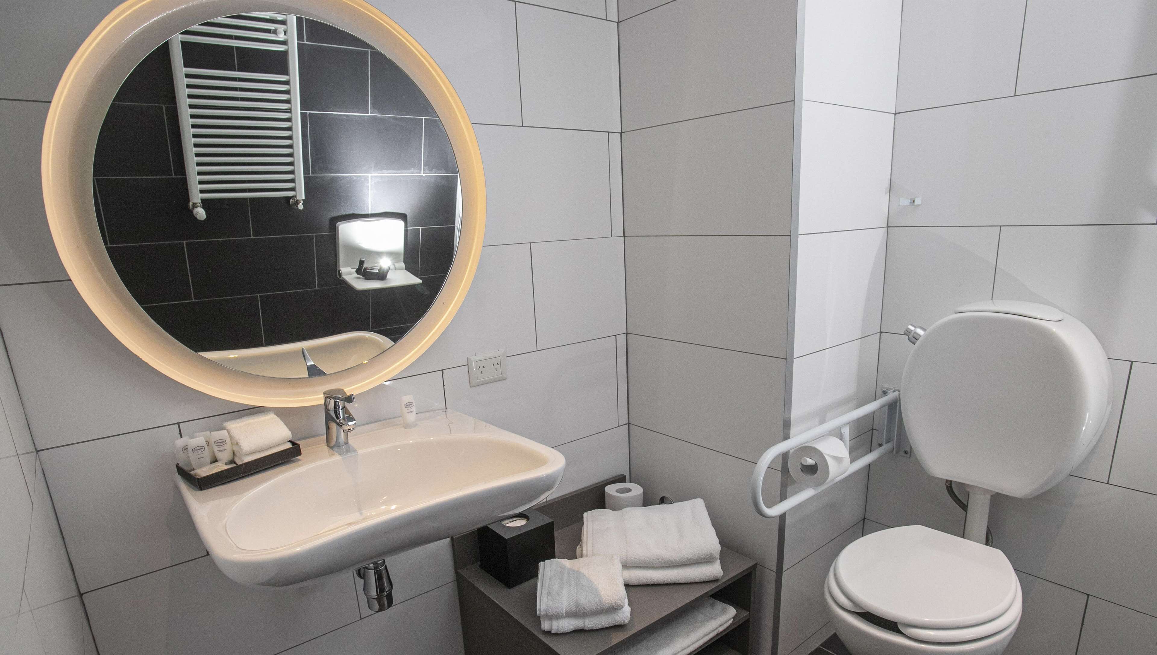 Un baño moderno con un espejo redondo, lavamanos blanco y retrete.