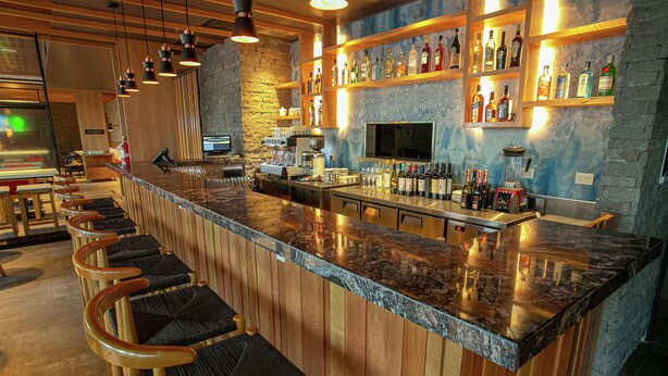 A bar area with a long counter, multiple stools, and shelves with bottles. - Hampton by Hilton Bariloche (San Carlos de Bariloche)