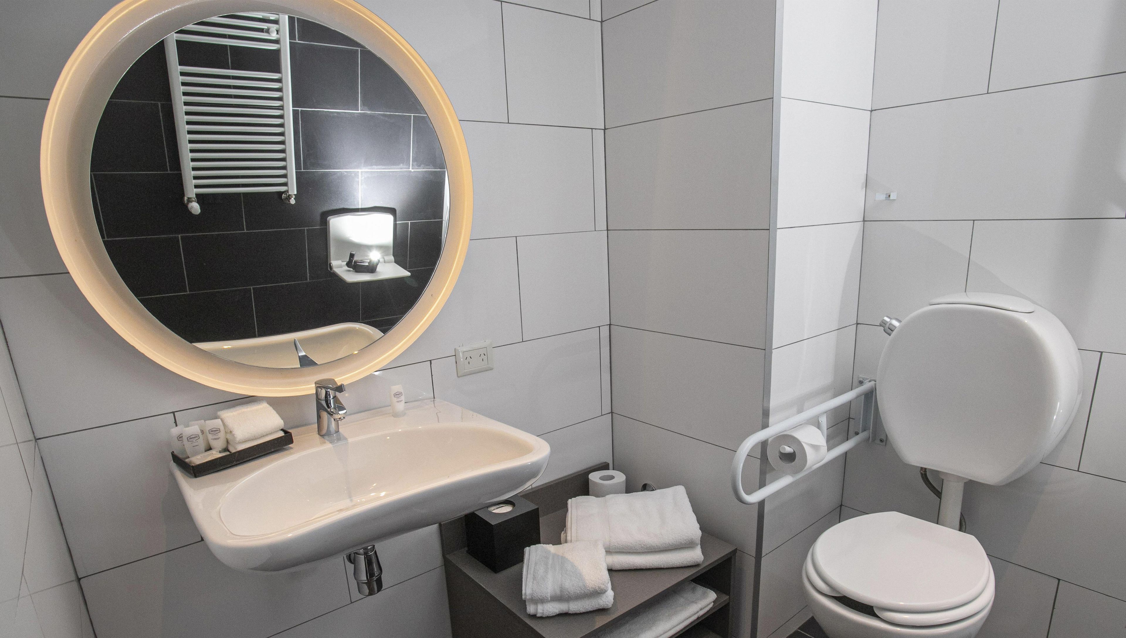 Ein modernes Badezimmer mit rundem Spiegel, weißem Waschbecken und Toilette.