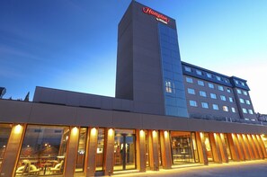 A modern hotel with a prominent Hampton by Hilton sign, large glass windows, and a well-lit entrance.