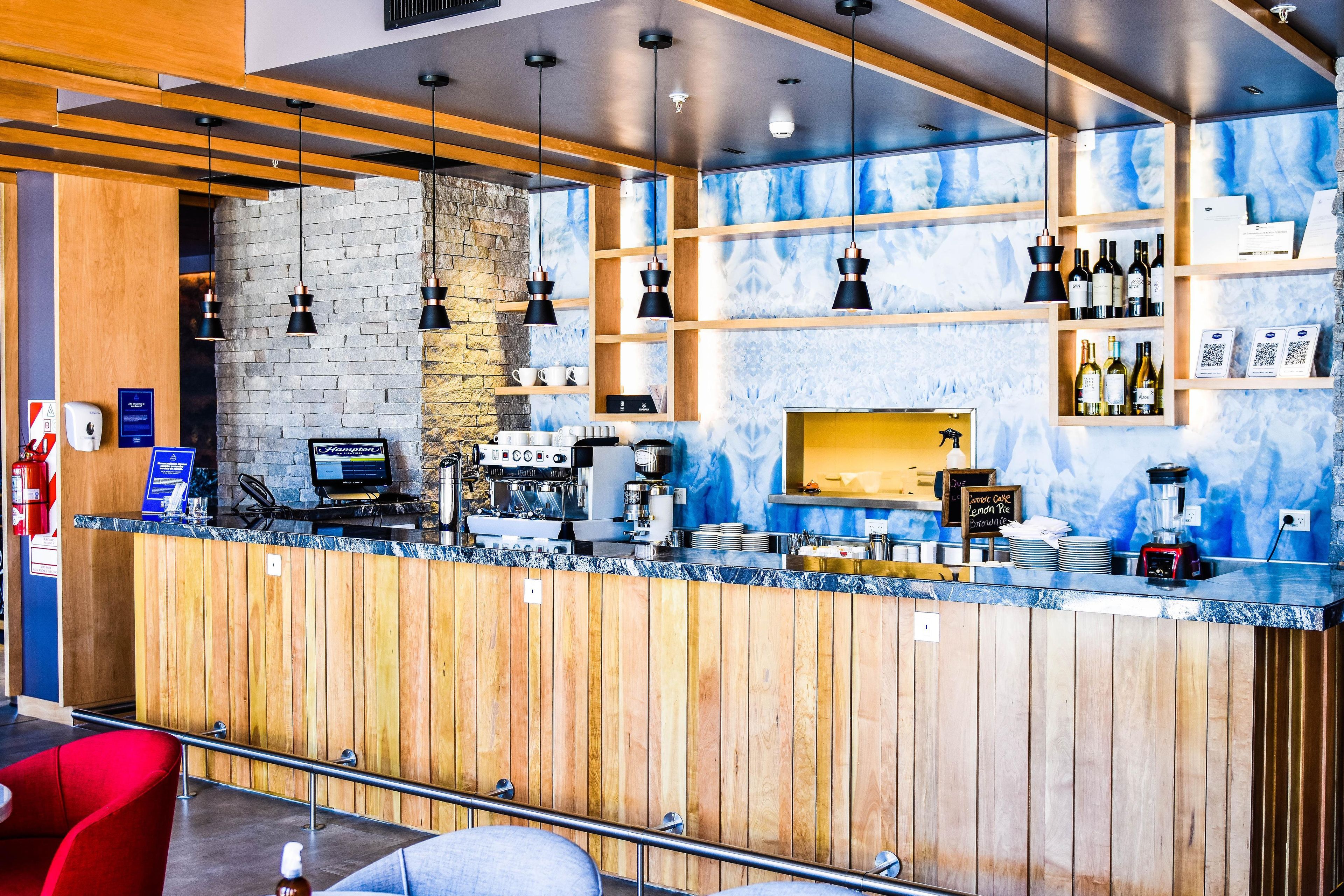 A modern bar area with a wooden counter, espresso machine, and wine bottles.