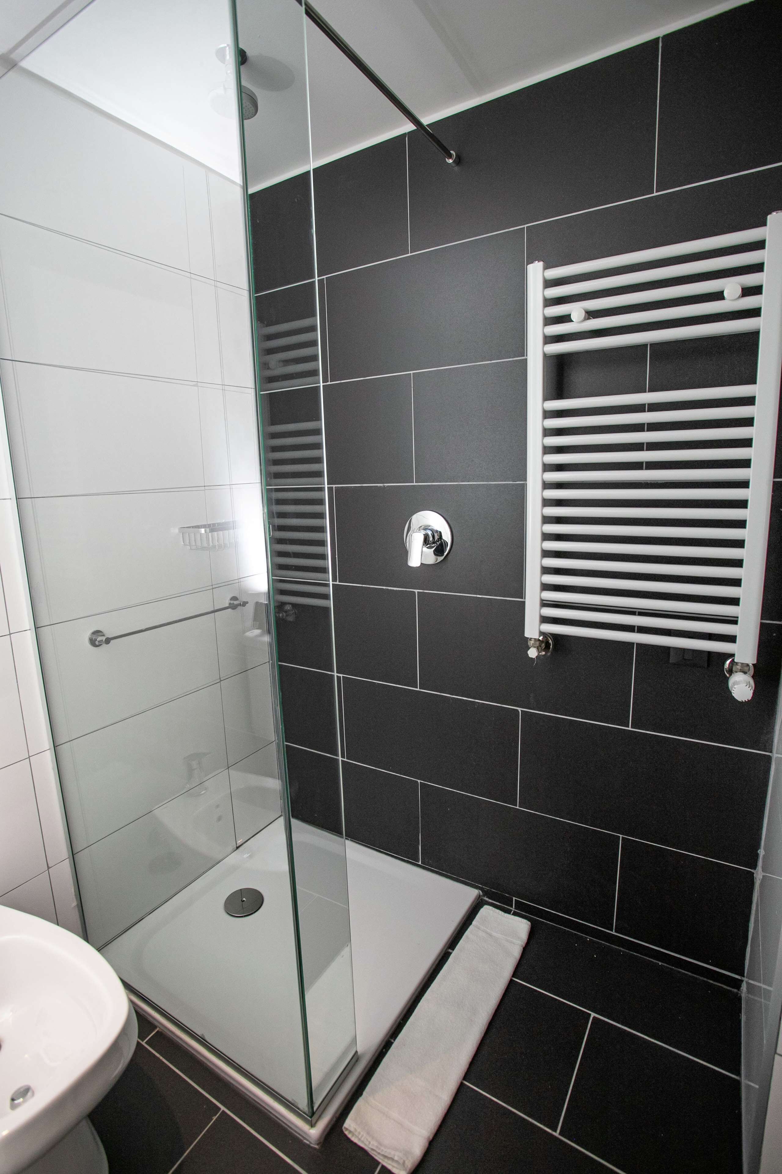 A modern bathroom with a glass shower enclosure, a white sink, and a towel rack on a dark tiled wall.