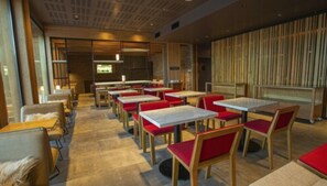 A restaurant interior with multiple tables and chairs, a wooden ceiling, and a view through a large window.