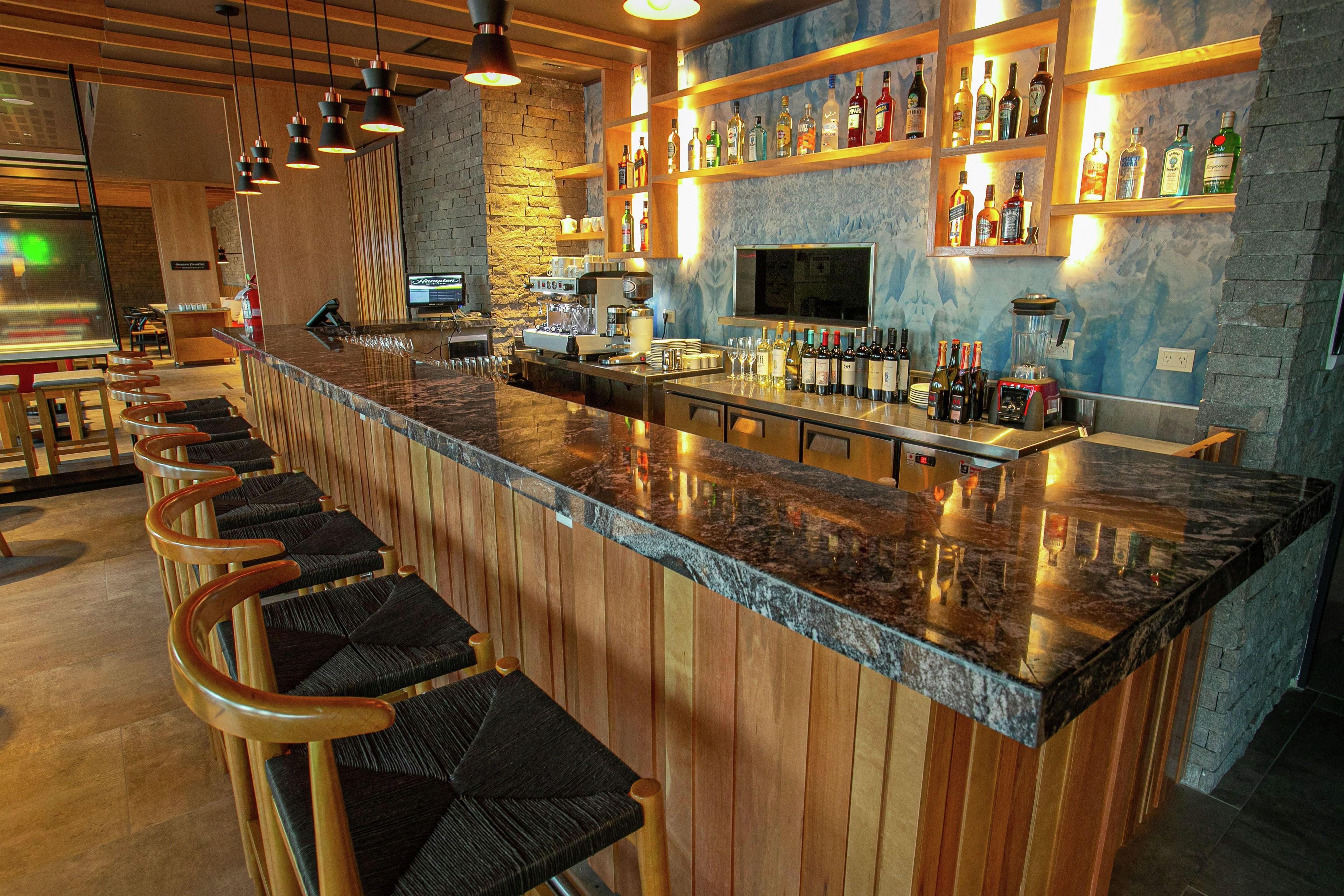 A bar area with a long counter, bar stools, and shelves with bottles.