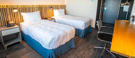 Una habitación de hotel con dos camas, un escritorio, una silla y un cabecero de madera.