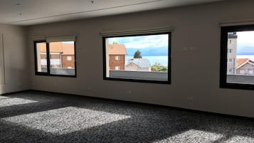 A spacious room with a large window, carpeted floor, and a view of buildings and a body of water.