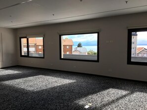 Una habitación amplia con un gran ventanal, piso alfombrado y vistas a edificios y una masa de agua.