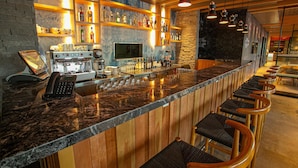 A bar area with a long counter, bar stools, a coffee machine, and shelves with bottles. - Hampton by Hilton Bariloche (San Carlos de Bariloche)