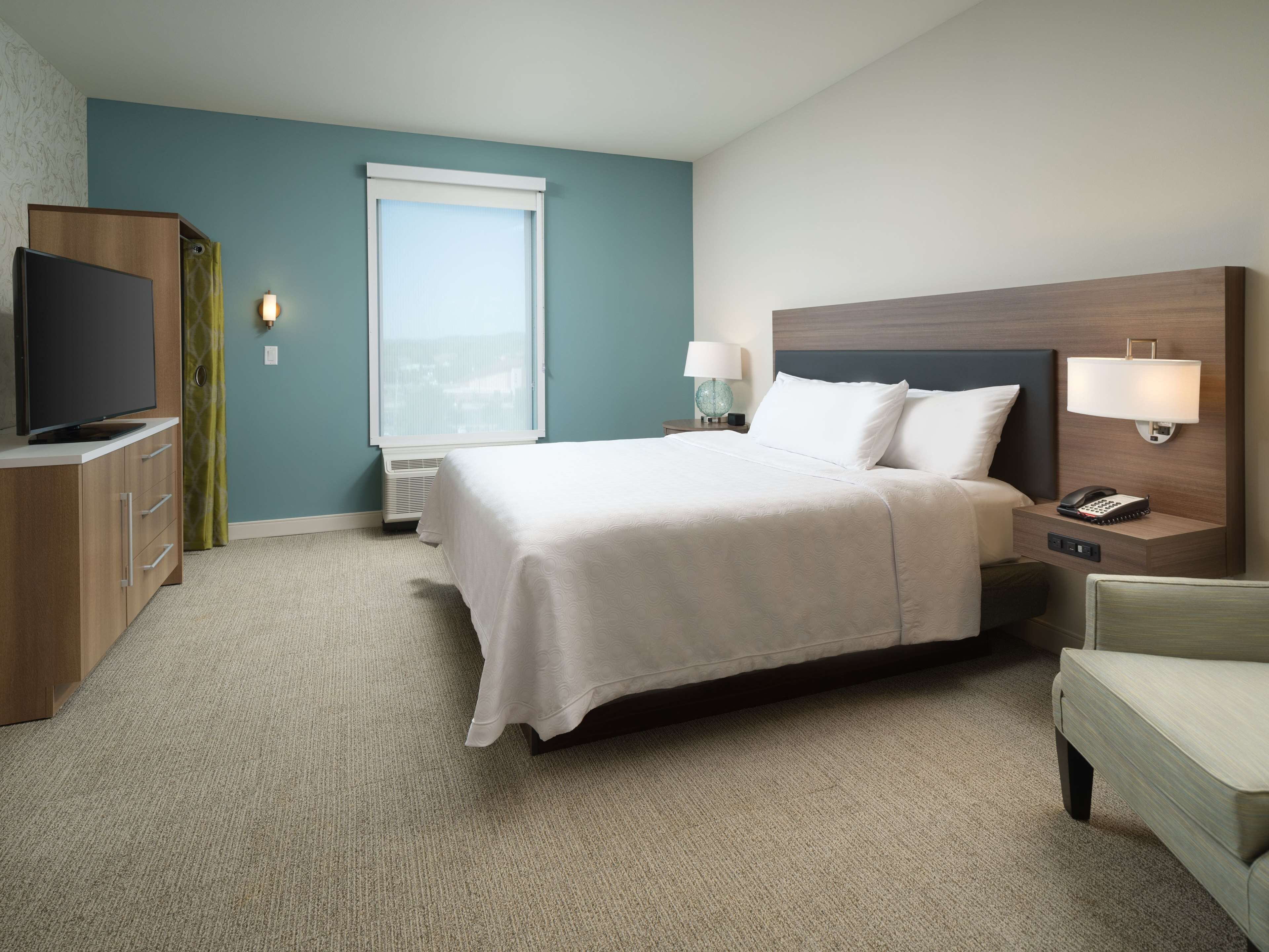 A hotel room with a bed, bedside tables, a TV, a window, and a view of the city.