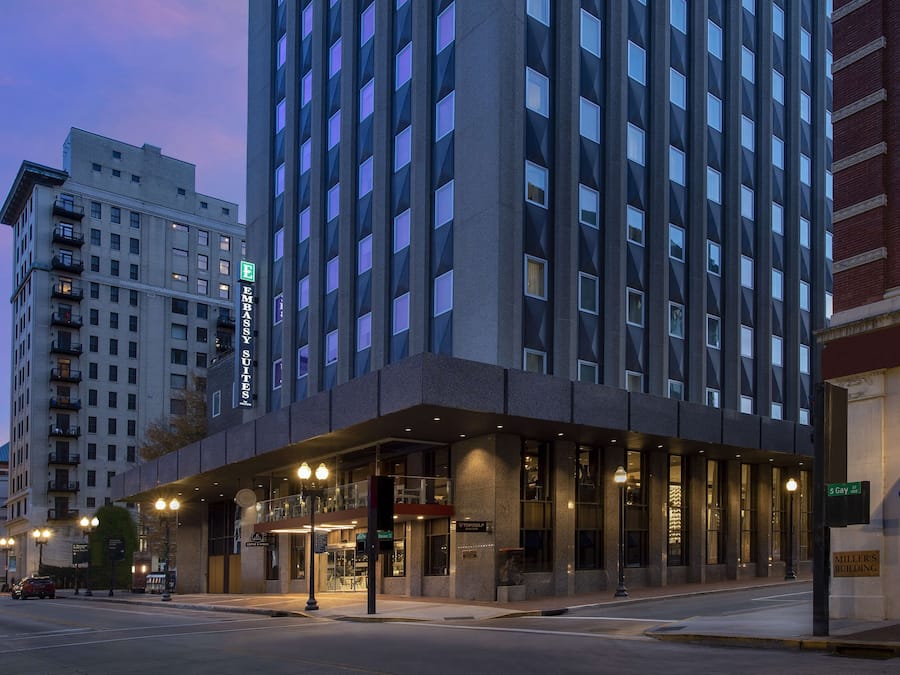 Un hotel moderno con un'imponente insegna a forma di 'E' per 'Eames Suites' sulla facciata, un ingresso a livello strada con area coperta e una targa che indica 'Miller's Building' a destra.