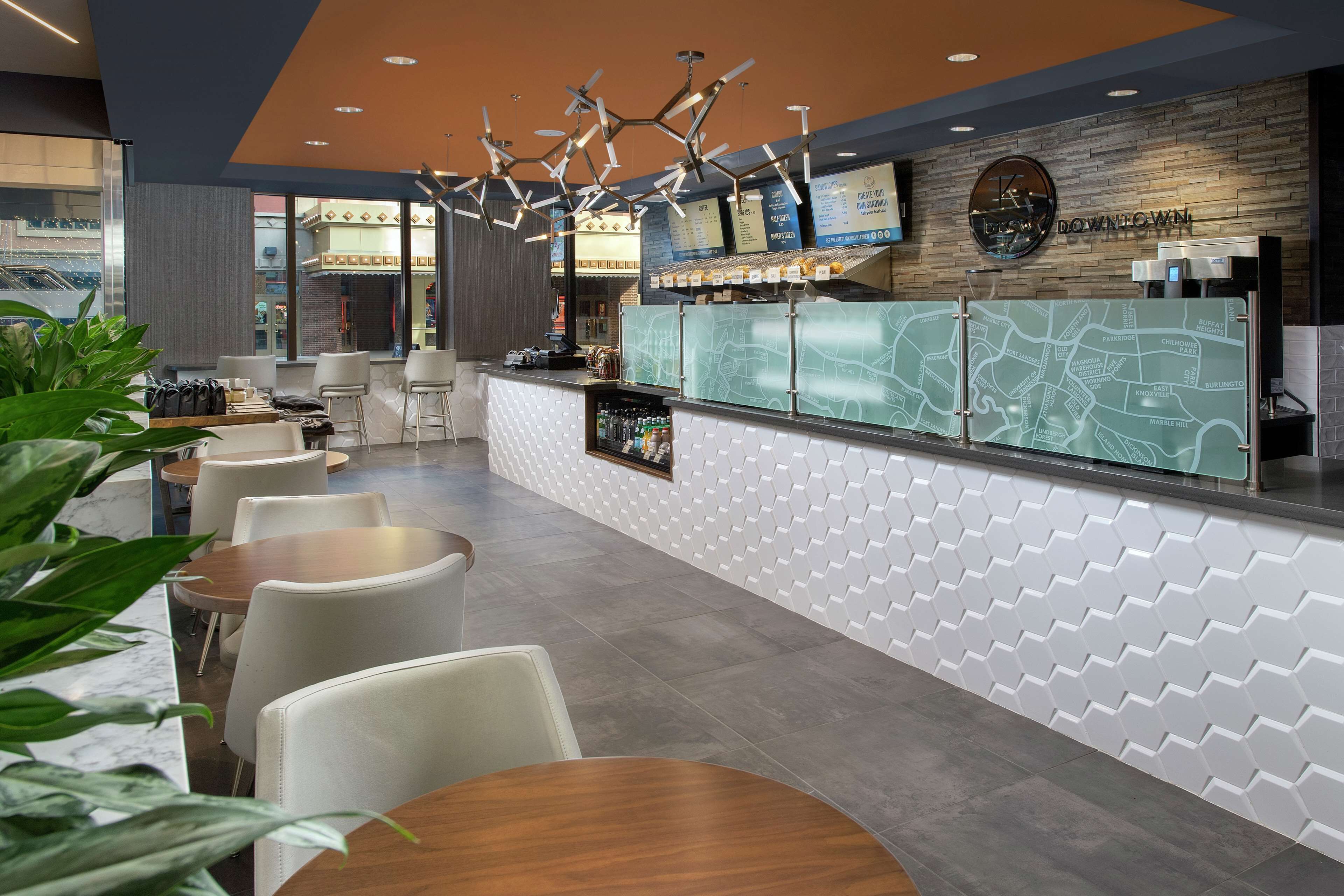 A modern hotel lobby with a reception desk, seating area, and a large window overlooking an outdoor space.