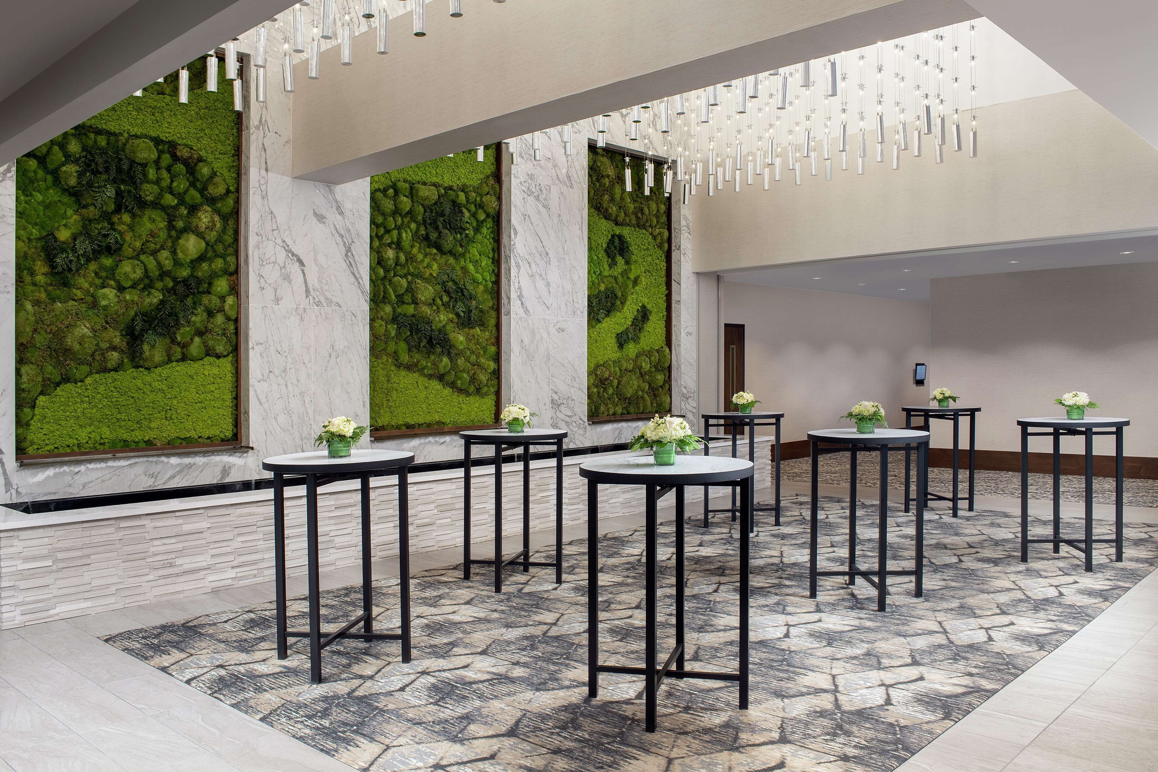 A modern lobby with marble walls, green moss walls, and black tables with potted plants.