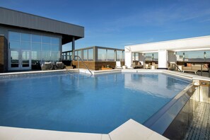 Ein moderner Poolbereich mit klarem, blauem Wasser, großen Fenstern und Außenmöbeln.