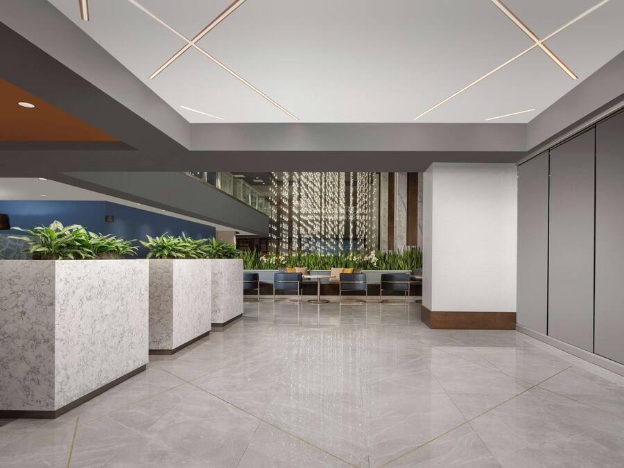 Een moderne lobby met marmeren receptiebalies, een zithoek en een decoratieve wand met verticale elementen.