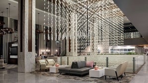 Un lobby amplio con un diseño moderno, que incluye un conjunto de sofás grises, mesitas blancas y una lámpara decorativa colgante.