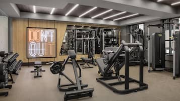 A modern gym with various weightlifting equipment, a motivational neon sign, and a large mirror.