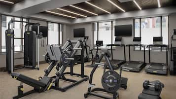 Un gimnasio moderno con diversos equipos de ejercicio, ventanas amplias y un televisor de pantalla plana.