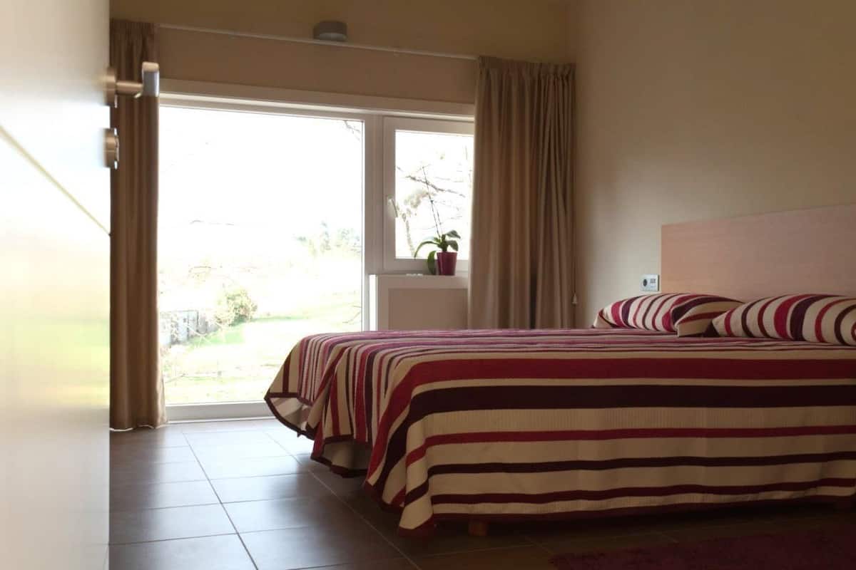 A bedroom with a bed, curtains, a window, and a view of the outdoors.