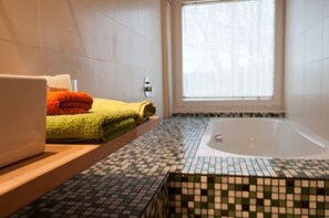 Un baño con piso de baldosas, una bañera y una ventana con cortinas.
