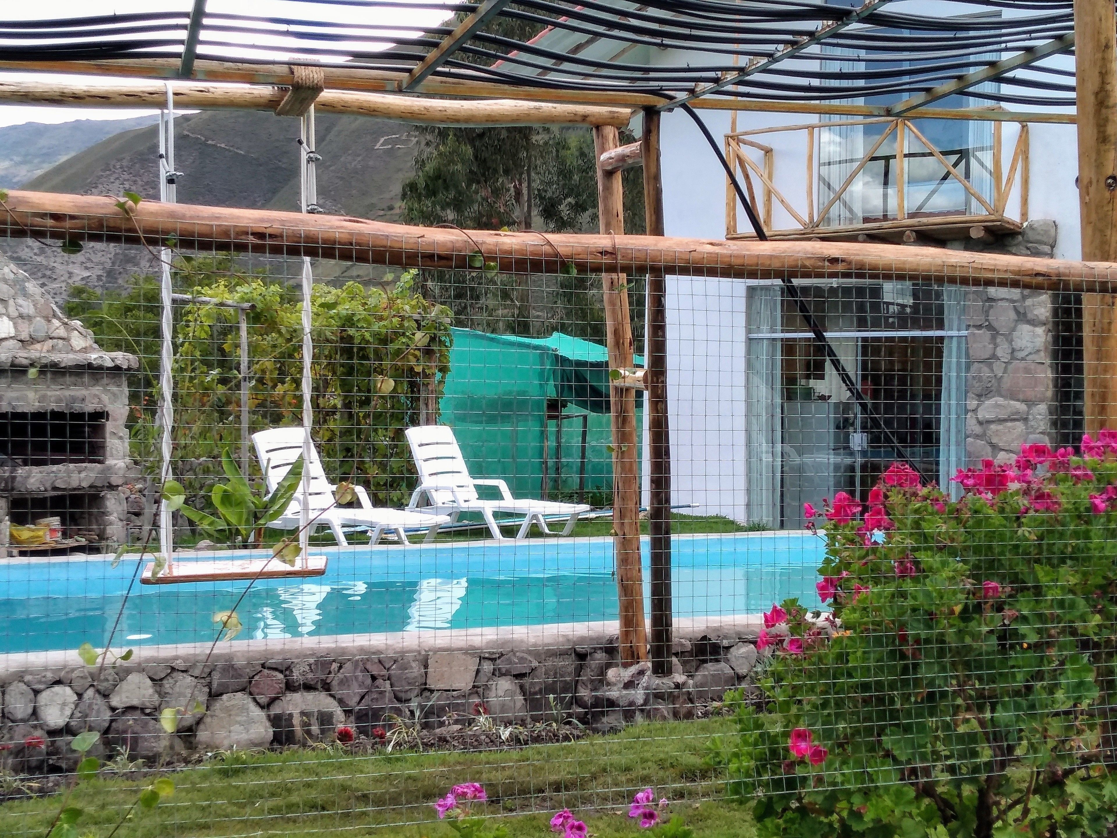 A pool area with a wooden swing bridge, white lounge chairs, and a stone wall.
