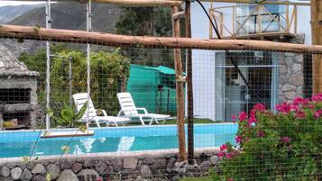 A pool area with a wooden swing bridge, white lounge chairs, and a stone wall.