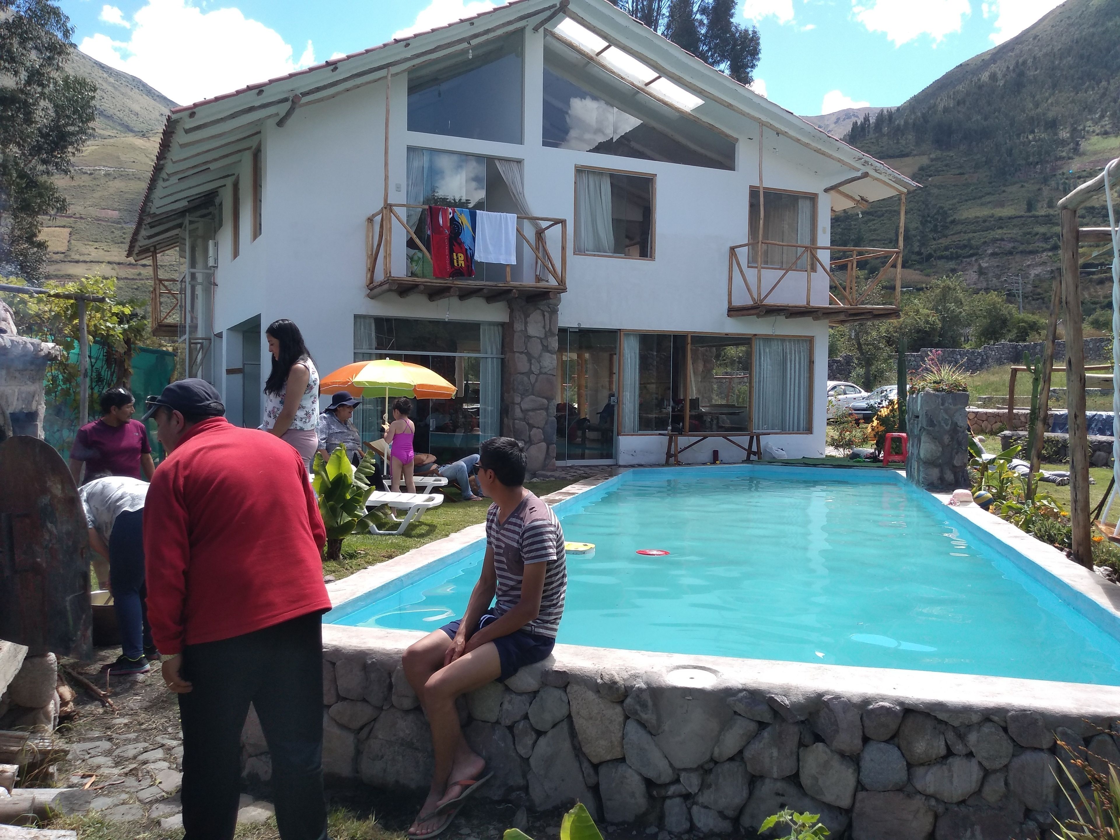 A two-story house with a swimming pool, stone walls, and a balcony with clothes hanging.