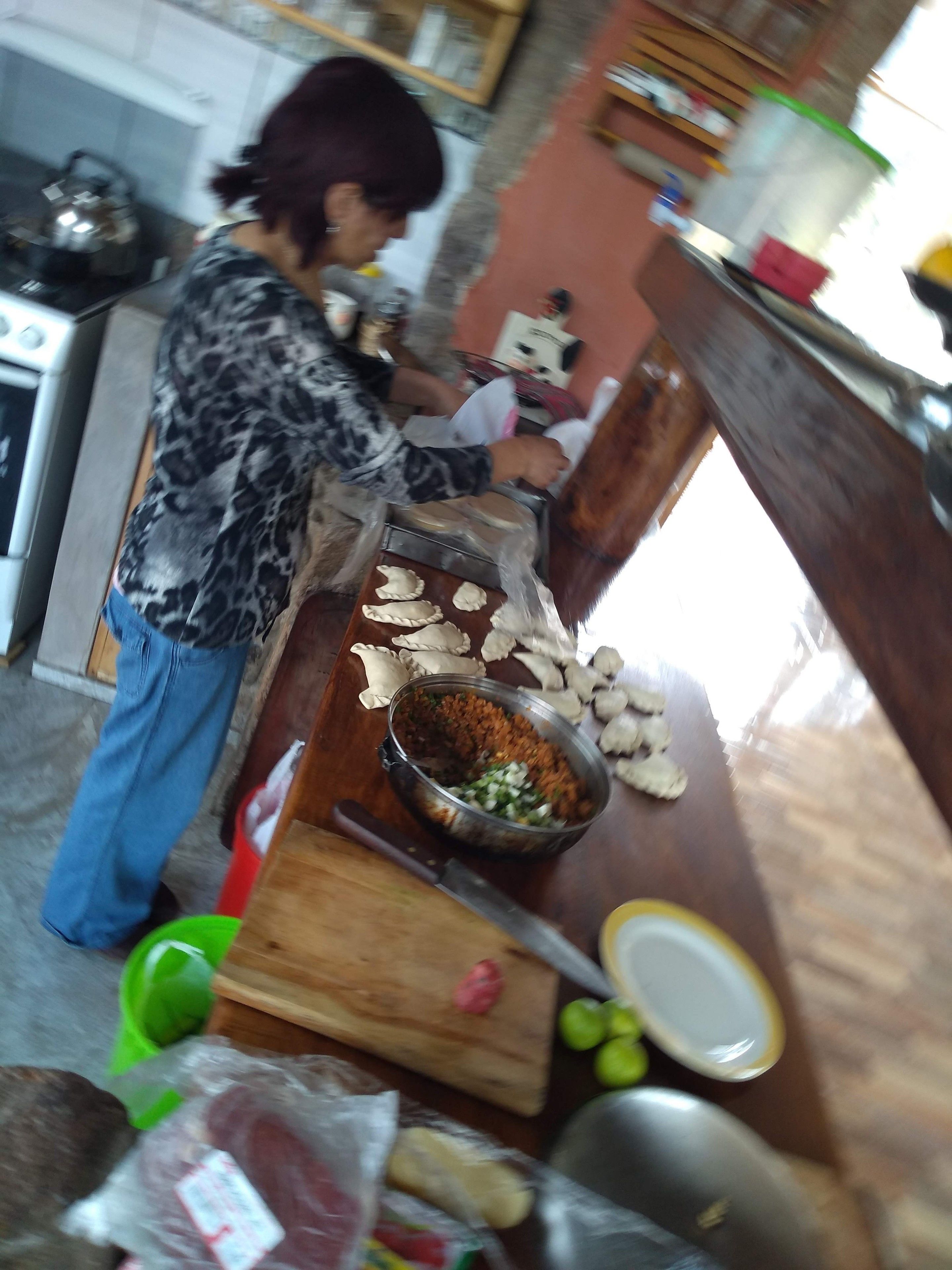 Una cucina con una persona che prepara cibo, un fornello, un tagliere e diversi utensili da cucina.