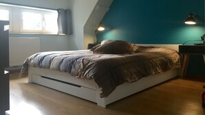 Una camera da letto con un letto, due lampade ai comodini, una finestra con tende e un soffitto spiovente.