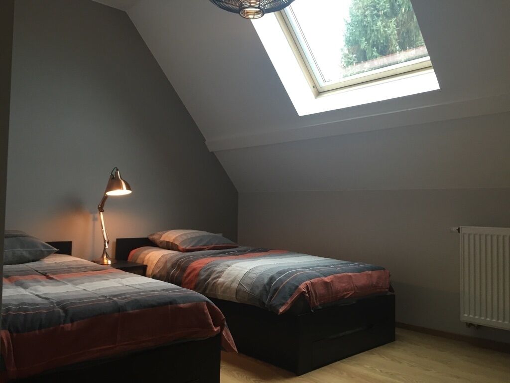 Une chambre avec deux lits, un puits de lumière, un radiateur et une lampe de bureau.