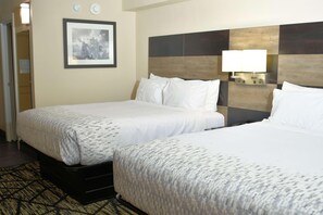 A hotel room with two beds, a framed picture on the wall, and a lamp on the headboard. - Clarion Pointe Jacksonville Near Camp Lejeune (Jacksonville)