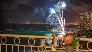 A table with two wine glasses and a bottle, overlooking a cityscape with fireworks in the distance. - Chic Studio w/Kitchenette, Lanai, AC, Washer/Dryer–Waikīkī Shore 304 (HONOLULU)