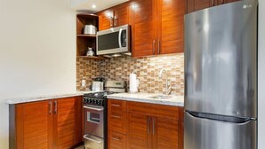 A modern kitchen with wooden cabinets, a stainless steel refrigerator, a microwave, and a stove. - Chic Studio w/Kitchenette, Lanai, AC, Washer/Dryer–Waikīkī Shore 304 (HONOLULU)