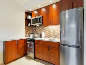 A modern kitchen with wooden cabinets, a stainless steel refrigerator, a microwave, and a stove.