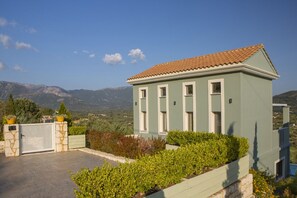 Un bâtiment à deux étages, doté d’un toit en tuiles, d’un portail en pierre et offrant une vue sur les montagnes en arrière-plan.