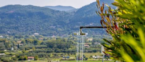 A waterfall with a metal spout, surrounded by lush greenery and a mountainous landscape in the background.