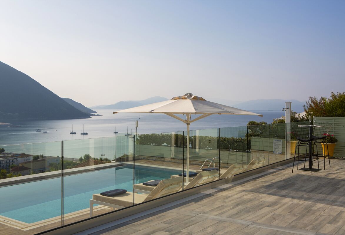 Una piscina a sfioro su un tetto, con schermi in vetro, poltrone da relax e ombrellone.